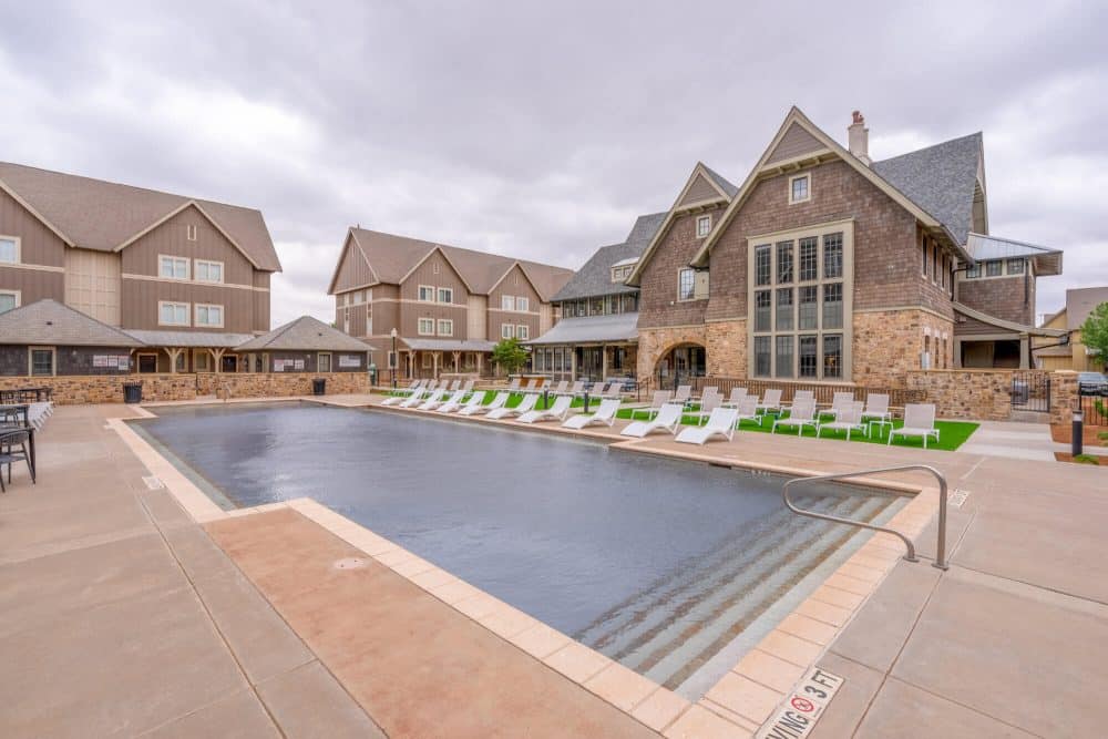 the collective at lubbock off campus cottage apartments pool with lounge chair seating on turf grass resident clubhouse building exterior